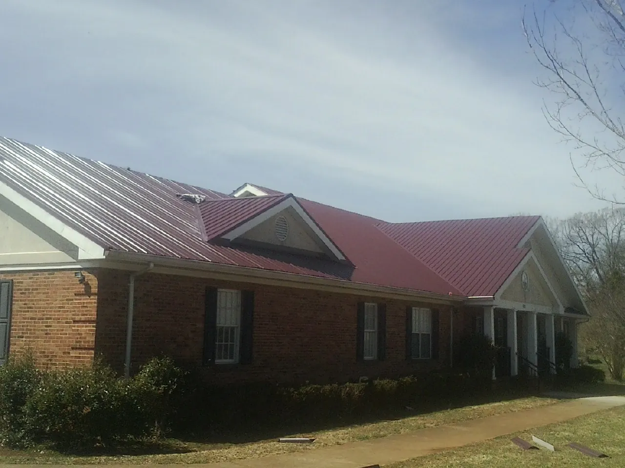 Red metal roof with gabled entries on a long brick building, from a Hail Damage Roof Repair job in Fort Loramie