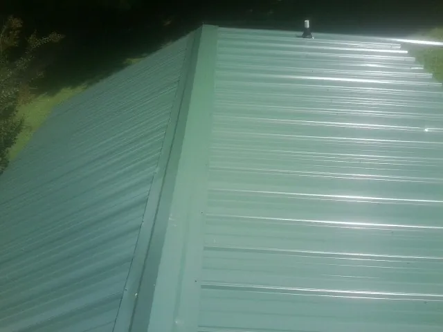 New green metal panels meeting at the ridge of a roof — Flat Roof Repair work by our crew in Fort Loramie