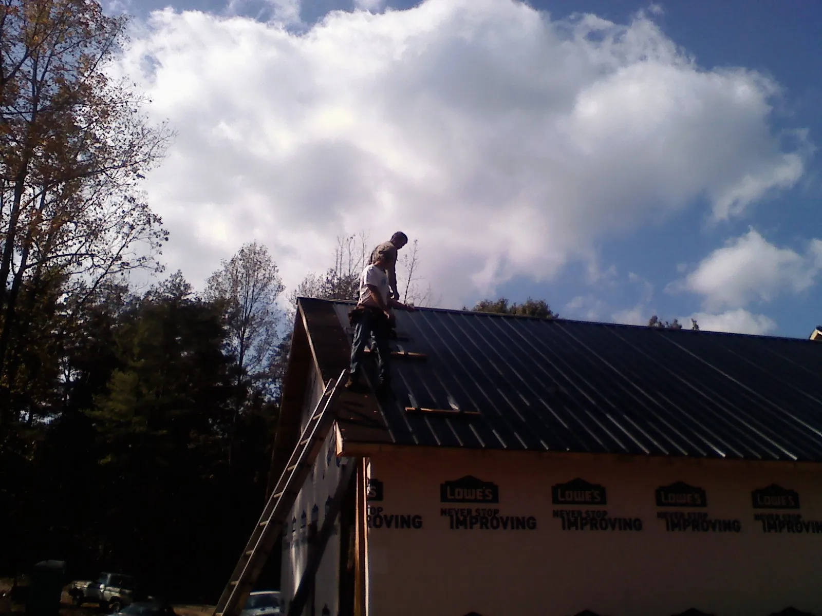 Roofer fastening dark metal panels high against a cloudy sky, from a Roof Inspection job in Fort Loramie