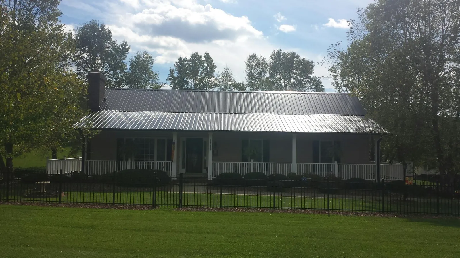 Gray metal roof on a brick ranch with a full width front porch — Gutter Guard Installation work by our crew in Fort Loramie