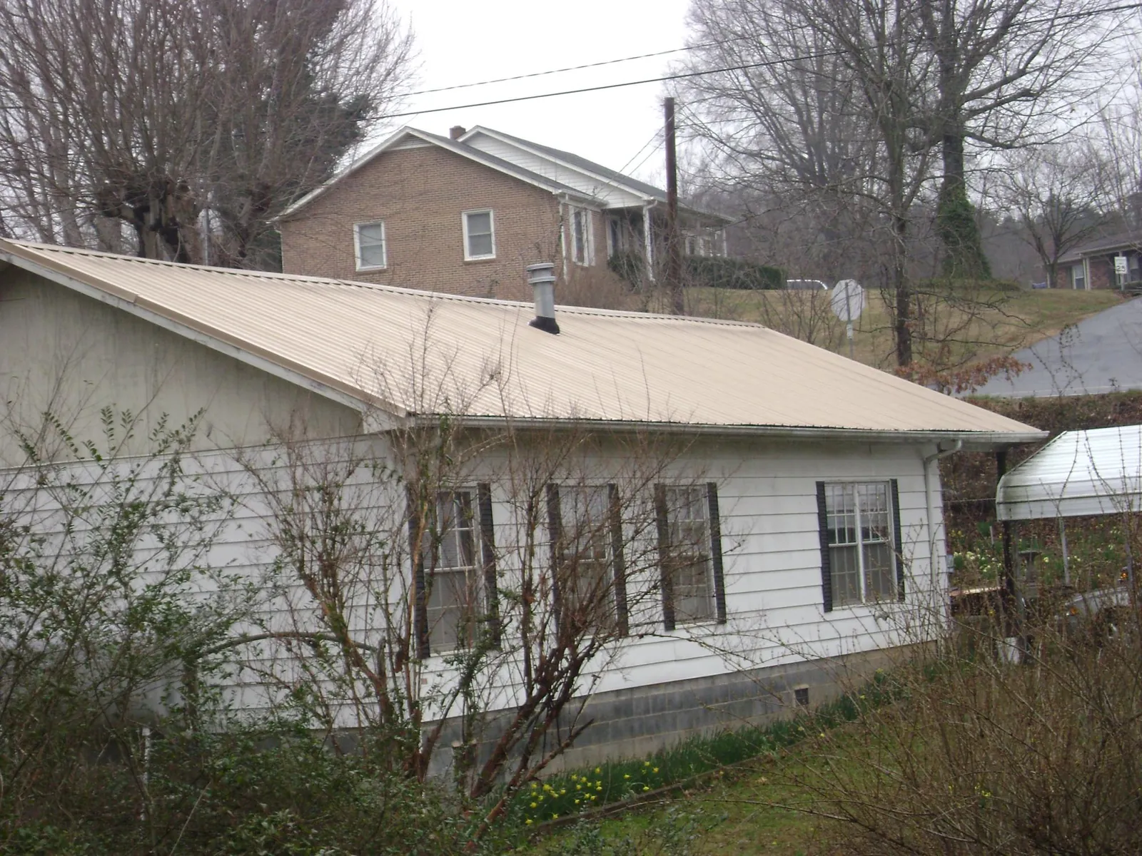 Tan metal roof on a white sided house set into a hillside — Commercial Roofing by Roofing Brothers in Fort Loramie