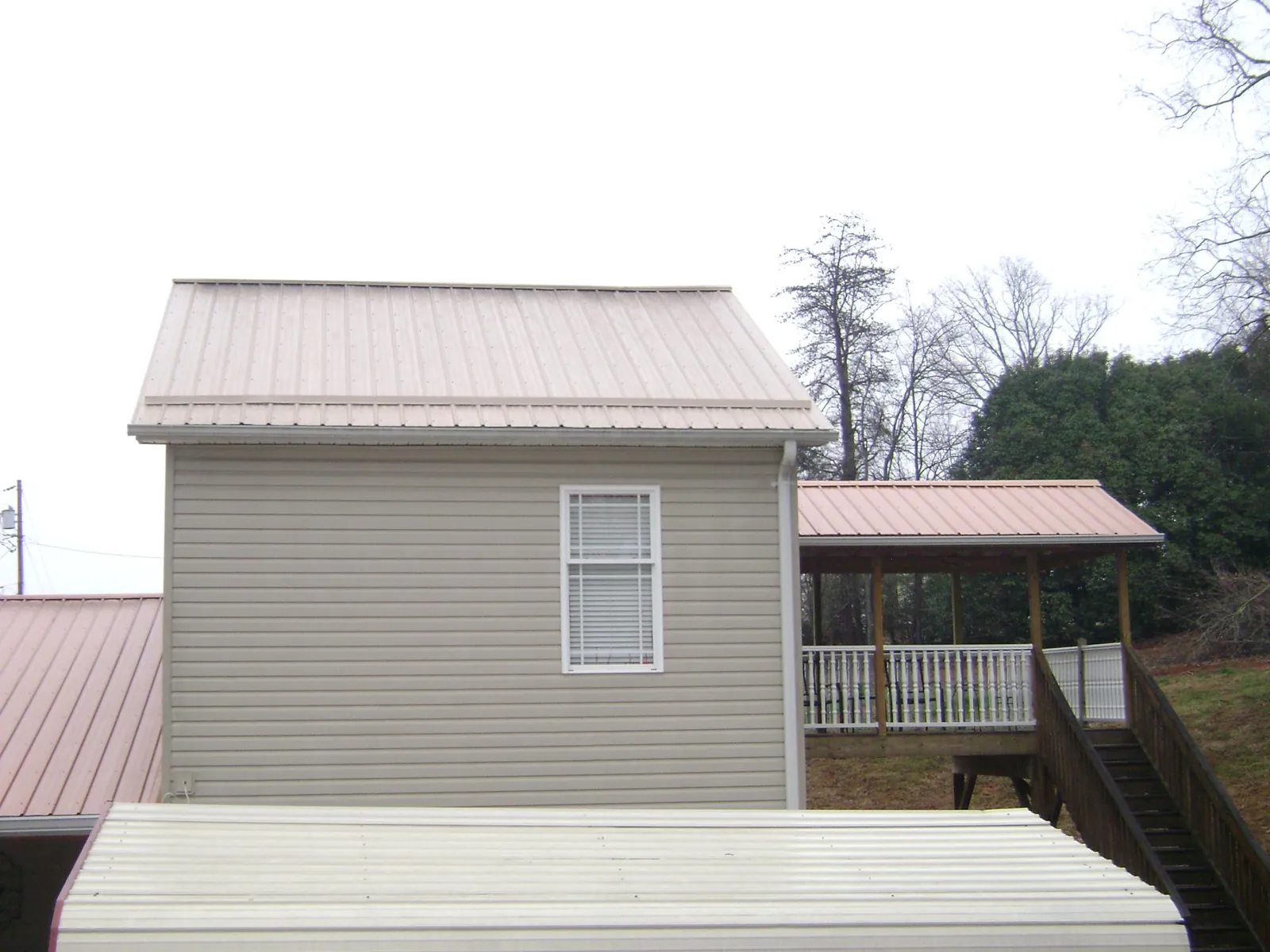 Tan metal roofs on a two story addition and attached porch, from a Roof Replacement job in Fort Loramie